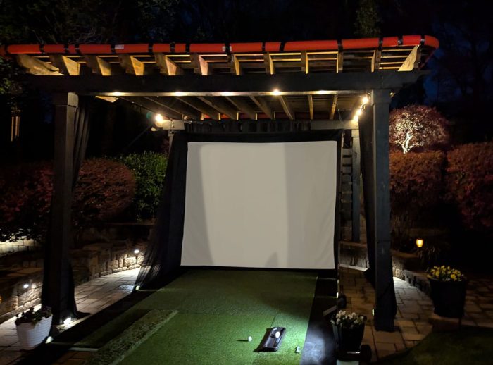 Projection Screen Outdoor Setup Outdoor projector screen under a wooden pergola at night with landscape lighting.