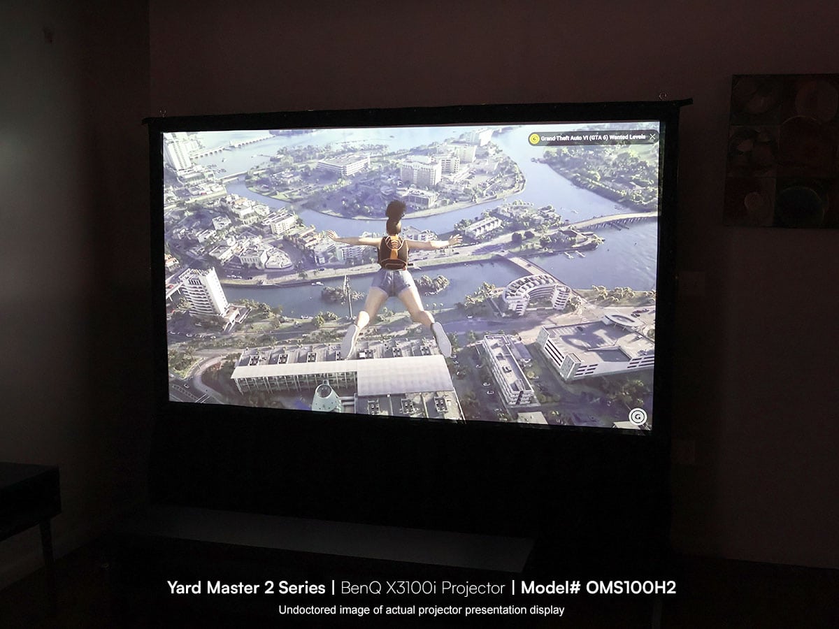 Large projector screen displaying a video game scene with a character hanging over a cityscape.