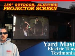 Outdoor electric projector screen with a man in sunglasses in front.